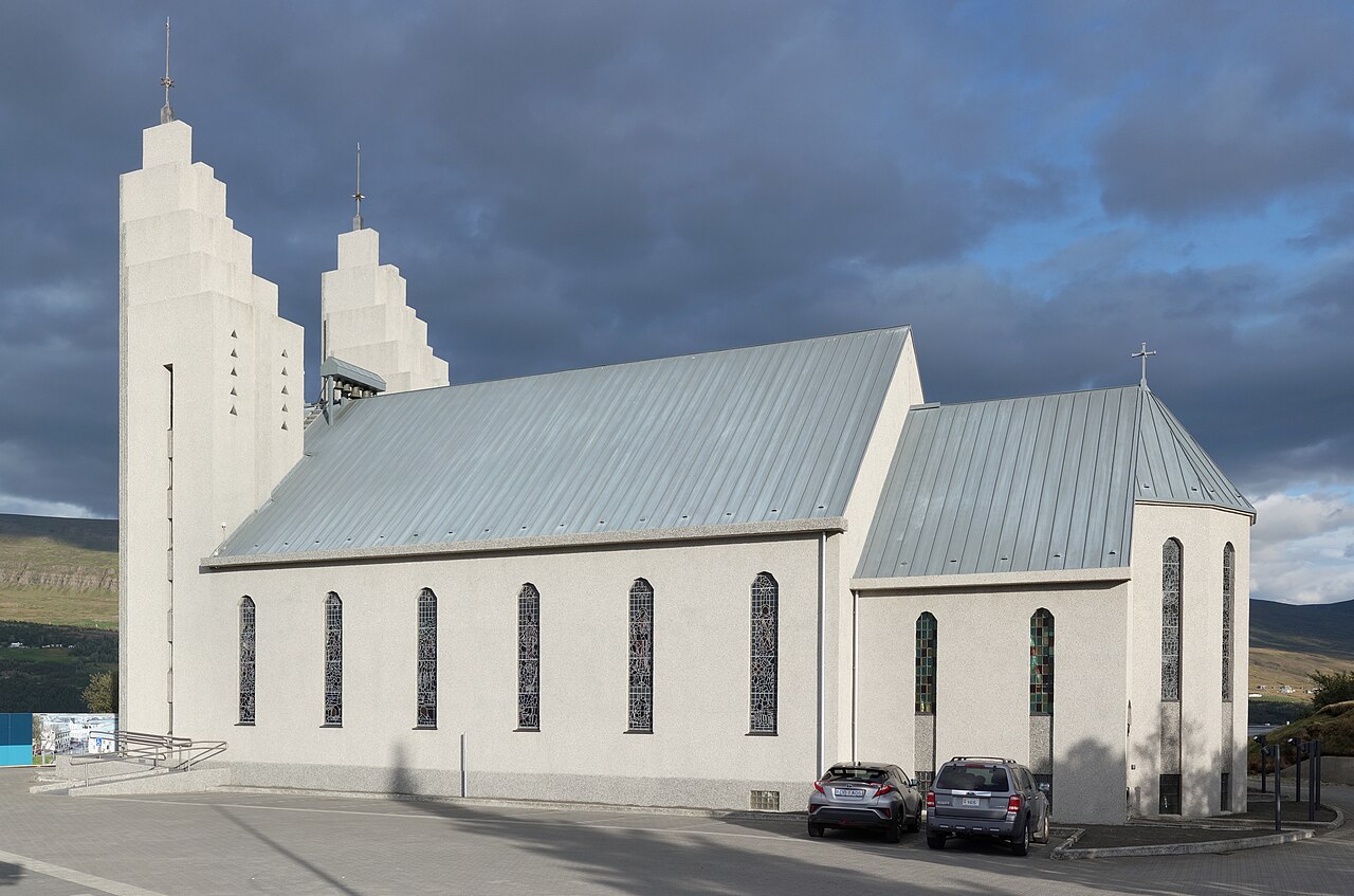 The twin towers and long side wall of Akureyrarkirkja under a cloudy sky.