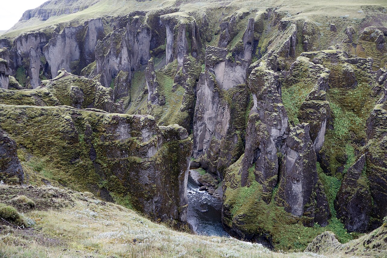A narrow river runs between tall, deeply cut canyon walls covered in green vegetation.